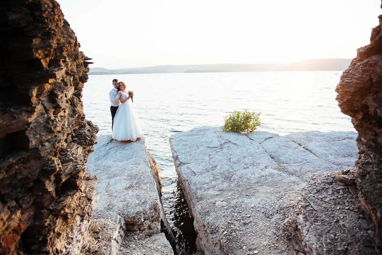 beautiful gorgeous blonde bride and stylish groom on rocks, on the background of a sea